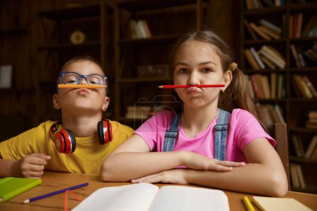 Photo for Portrait of cute children holding pencil on mouth under nose. Mischief humor boy and girl siblings feeling playful and fooling around. Happy childhood and interesting home education - Royalty Free Image