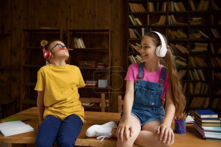 Photo for Happy children enjoying studying and happy time on homeschooling. Brother and sister sitting on table wearing headphones fooling around feeling joyfulness and excitement - Royalty Free Image
