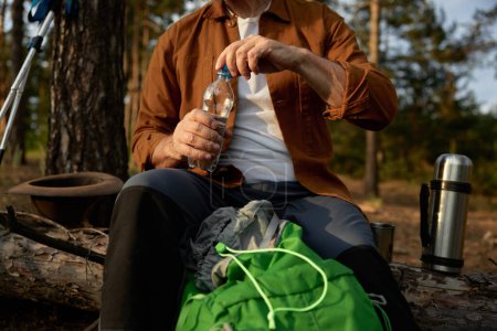 Foto de Senderista masculino mayor o explorador del desierto tomando un descanso y beber agua durante el senderismo en el bosque de pinos. Disfrutar de la expedición en la jubilación - Imagen libre de derechos