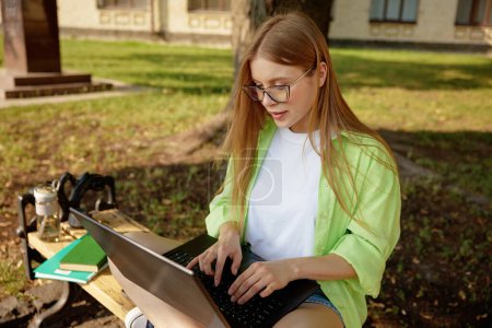 Photo for Confident female student working on laptop computer outdoors. Freelancing and learning online, preparation for exam or homework studying - Royalty Free Image