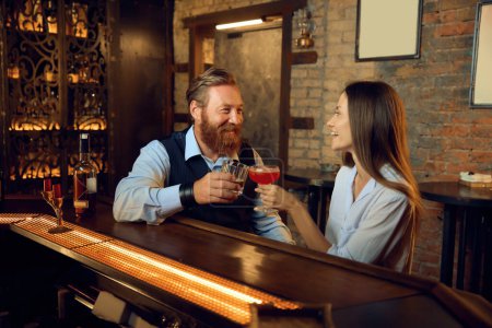 Photo for Handsome man and young woman rest together in bar talking while sitting at bar counter. Friendly conversation and flirting - Royalty Free Image