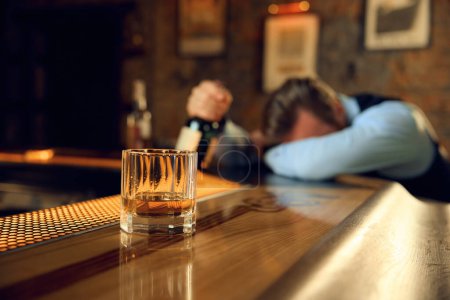 Photo for Drunk man sleeping at bar counter with focus on alcoholic drink in glass. Stressed day and alcohol addiction concept - Royalty Free Image