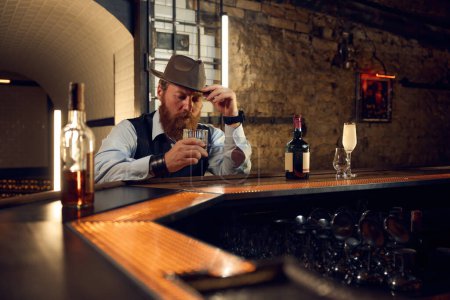 Téléchargez les photos : Portrait d'un gentleman mature dans un verre au comptoir du bar. Élégant homme à l'ancienne qui boit des boissons alcoolisées dans un bar - en image libre de droit