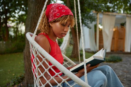 Photo for Young woman reading book while rest on hanging wicker chair. Holiday vacation on nature during summertime - Royalty Free Image