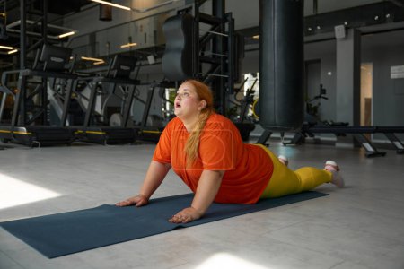 Téléchargez les photos : Femme obèse appréciant la routine d'étirement après un entraînement dur abdos croquant. Entraînement de fitness au gymnase sportif concept - en image libre de droit
