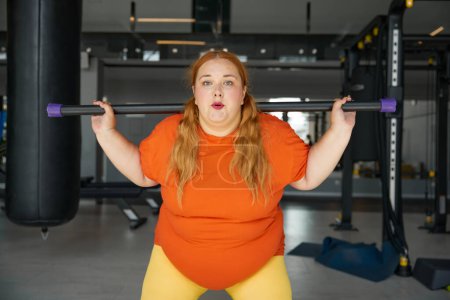 Photo for Overweight woman having fitness workout squatting with body bar training equipment. Obese girl exercising for being strong, slim and healthy - Royalty Free Image