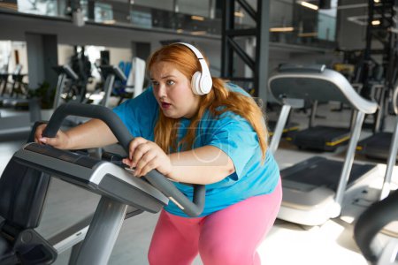 Photo for Crazy motivated overweight woman riding fast on stationary bike in gym. Fitness class for obese people concept - Royalty Free Image