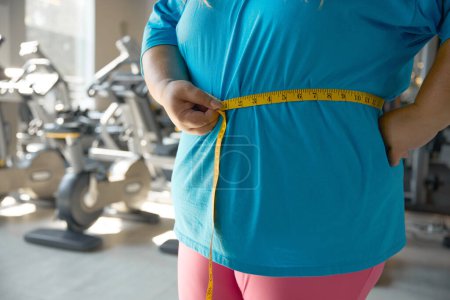 Photo for Closeup waistline of chubby woman wrapped in measuring tape. Workout sport and slimming program for people with obesity - Royalty Free Image