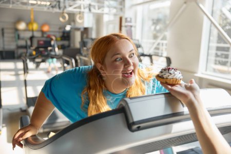 Photo for Closeup front view on face of obese woman at gym reaching to donut with hands. Choice between sport for slimming and unhealthy food with obesity - Royalty Free Image
