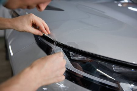 Photo for Worker detailer cutting off excess of polymer protective outer coating at car headlight. Closeup on hand of car service master - Royalty Free Image