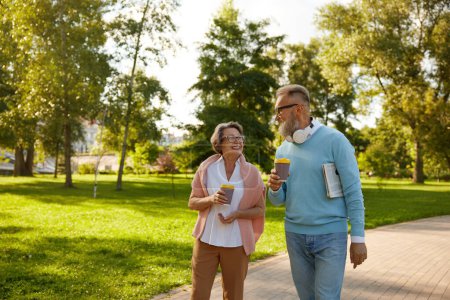 Photo for Happy fashioned elderly couple having coffee break walking in park. Romantic aged mature man and woman looking happy enjoying healthy lifestyle on pension - Royalty Free Image