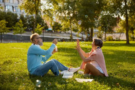 Photo for Playful active senior couple blowing soap bubbles while rest in park. Vitality and active elderly people concept - Royalty Free Image