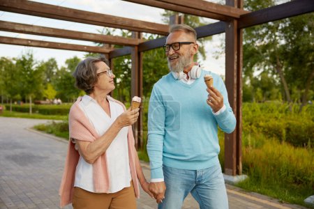 Téléchargez les photos : Joyeux couple de personnes âgées mangeant un cône de crème glacée dans le parc en profitant du temps de détente. Joyeux mode de vie des personnes âgées, temps de pension ensemble concept - en image libre de droit