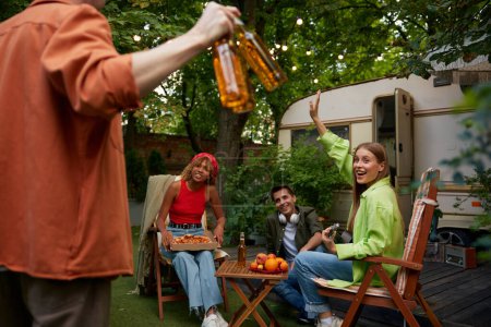Téléchargez les photos : Groupe d'amis heureux se reposant dans RV camping à proximité de leur camping-car dans la forêt - en image libre de droit