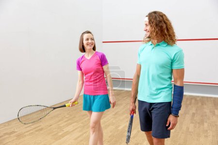 Foto de Joven hombre y mujer vestidos con ropa deportiva preparándose para el partido de squash en el club de entrenamiento indoor - Imagen libre de derechos