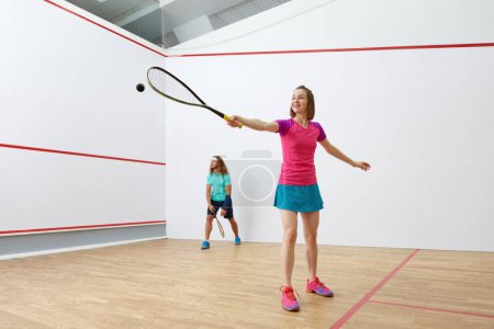 Foto de Feliz millennial-age pareja de personajes jugando juego de racquetball juntos. Jugadores de squash entrenando juntos en pista cubierta - Imagen libre de derechos