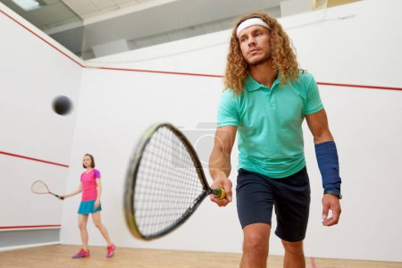 Squash male player with racket playing game with female friend at indoor training court