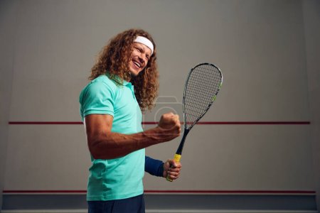 Téléchargez les photos : Portrait de joueur de squash satisfait serrant poing se réjouissant victoire dans le jeu ou fin réussie de l'entraînement - en image libre de droit