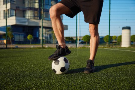 Photo for Crop view if man holding foot on soccer ball standing over football field. Training favorite game outdoor - Royalty Free Image