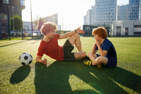 Foto de Papá e hijo teniendo una agradable conversación después de la actividad recreativa de entrenamiento de fútbol mientras descansan en el campo de fútbol al aire libre - Imagen libre de derechos