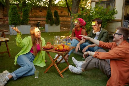 Téléchargez les photos : Groupe d'amis millénaire divers jouant jeu drôle près de remorque s'amuser ensemble pendant le pique-nique en plein air. Concept de voyage camping - en image libre de droit