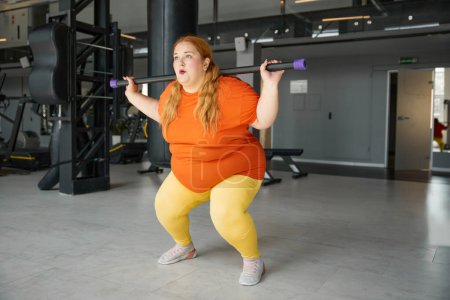 Photo for Overweight woman having fitness workout squatting with body bar training equipment. Obese girl exercising for being strong, slim and healthy - Royalty Free Image