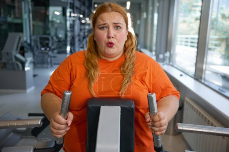 Photo for Portrait of tired sweaty obese woman working on elliptical machine. Intense cardio workout at gym - Royalty Free Image
