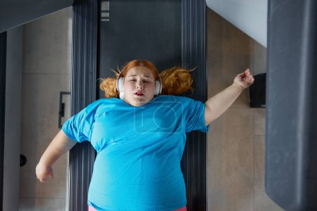 Foto de Triste infeliz mujer con sobrepeso que siente dolor en la espalda mientras entrena en la pared para la corrección de la postura. Chica obesa divertida llorando mirando con desesperación en la cara - Imagen libre de derechos