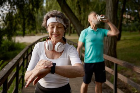 Photo for Senior fitness woman proud of overtaking her tired husband during morning running workout. Retiree cardio wellness or marathon jog - Royalty Free Image