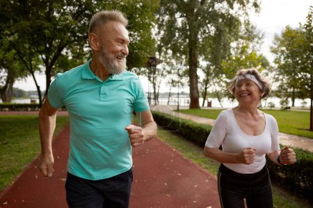 Photo for Senior couple running on track together outdoor at natural park. Happy healthy elderly woman and mature man friends exercising outdoors - Royalty Free Image