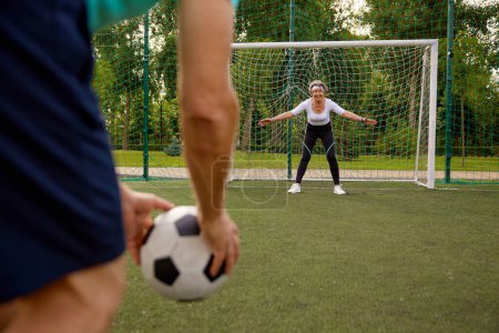 Téléchargez les photos : Femme âgée debout aux portes se préparant à attraper le ballon de football. Couple heureux de personnes âgées jouant au football ensemble à l'extérieur - en image libre de droit