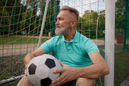 Photo for Happy senior man feeling tired after football training on soccer field. Sweaty exhausted elderly sportsman rest during recreational pursuit outdoors - Royalty Free Image