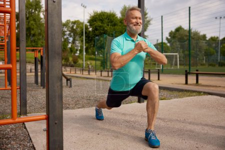 Foto de Hombre mayor haciendo ejercicios físicos en el campo de deportes al aire libre. Entrenamiento de entrenamiento para personas mayores - Imagen libre de derechos