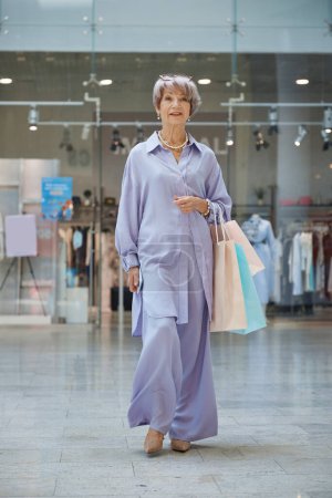 Téléchargez les photos : Portrait complet d'une séduisante femme âgée avec des sacs à provisions sur la vitrine du magasin. Élégant grand-mère se sentant satisfait profiter de réductions dans la boutique - en image libre de droit