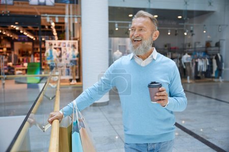 Téléchargez les photos : Un bel homme âgé qui va faire du shopping au magasin. Homme d'affaires âgé souriant se sentant satisfait de la grande journée à l'aéroport de détail - en image libre de droit