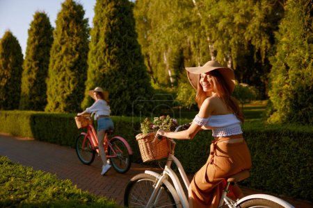 Photo for Stunning young females laughing riding bicycle and having fun in urban park. Excited positive teenager girls friends enjoying walk and summer season - Royalty Free Image