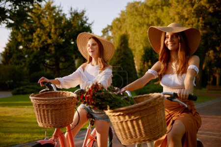 Téléchargez les photos : Joyeux jeune fille avec un ami féminin à vélo dans le parc. Fun étudiant loisirs et amitié gens relations - en image libre de droit