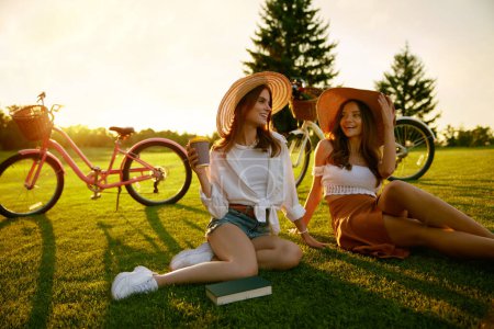 Foto de Dos jóvenes mujeres hipster descansando tomando un café después de una carrera en bicicleta activa. Relaciones de novias y fines de semana felices - Imagen libre de derechos
