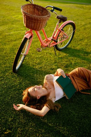 Téléchargez les photos : Portrait de jeune femme lisant un livre sur la nature faisant une pause pendant un voyage à vélo à l'extérieur. Temps libre, loisirs de loisir - en image libre de droit