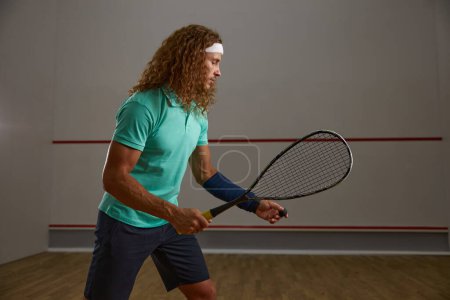 Photo for Young adult concentrated squash player practicing serve while exercising game at gym. Sportsman portrait - Royalty Free Image