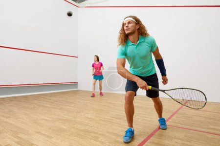 Téléchargez les photos : Joueur masculin de squash avec raquette jouant au jeu avec une amie au terrain d'entraînement intérieur - en image libre de droit