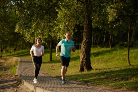 Photo for Lovely joyful retirees couple jogging outside in city park during early morning. Elderly man and woman enjoying cardio sports training - Royalty Free Image