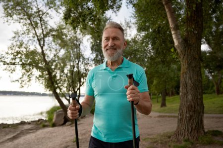 Téléchargez les photos : Portrait d'un homme âgé profitant de magnifiques paysages du parc lors d'une randonnée en été. Sportif mature âgé faisant la promenade de pôle sportif pour l'amélioration de l'endurance physique et des soins de santé - en image libre de droit