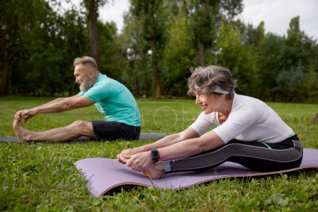 Photo for Happy senior couple doing yoga stretching exercise outdoors. Retirees training workout for health - Royalty Free Image