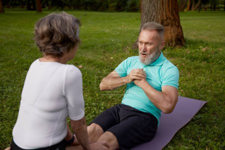Photo for Happy older couple of retirees doing training workout in park. Elderly wife helping senior husband doing abdominal crunch. Sports leisure activity for pensioner - Royalty Free Image