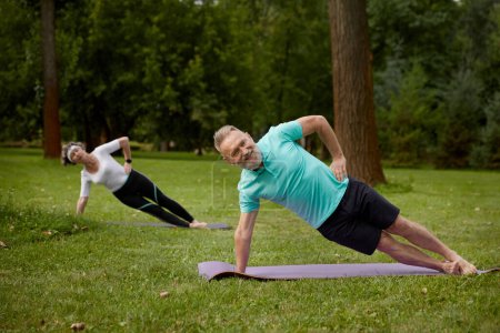 Téléchargez les photos : Couple âgé debout sur la planche latérale de l'exercice pour le bien-être à l'extérieur dans le parc. Activité famille âgée pratiquant le yoga pour l'endurance, la force et la santé - en image libre de droit