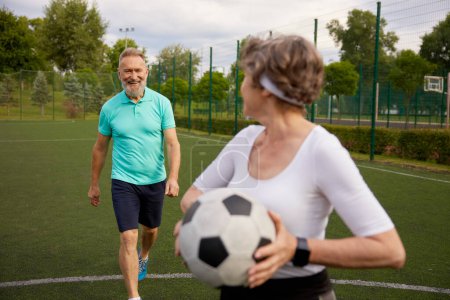 Photo for Happy elderly couple with football ball on sportive stadium in city park. Healthy habits of retired people - Royalty Free Image
