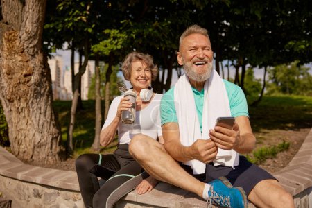 Téléchargez les photos : Heureux heureux heureux couple de personnes âgées et de femmes profitant d'une journée ensoleillée après avoir fait du jogging dans le parc. Activité sportive pour les personnes âgées et mode de vie sain concept - en image libre de droit