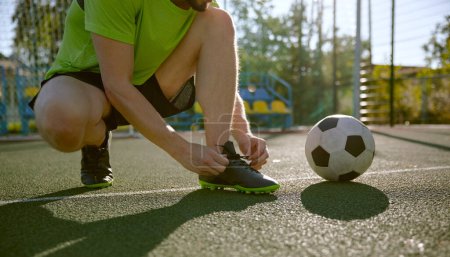 Photo for Amateur soccer player tying shoelaces before training closeup. Athlete ready to start football match with friends. Comfortable activewear for sport - Royalty Free Image
