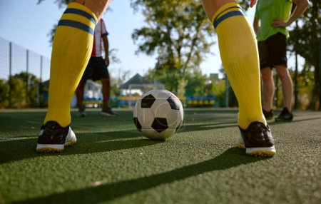 Photo for Closeup soccer ball and sportsman legs over grass football field. Male athlete feet wearing fitness shoes and stockings training clothing with footwear - Royalty Free Image